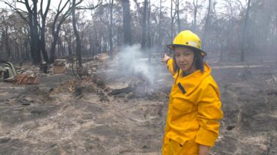 BBC's Sydney Correspondent Shaimaa Khalil stands amid burnt trees and flattened land in Balmoral, Australia.