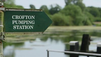 a green sign saying "Crofton Pumping Station" in front of a river