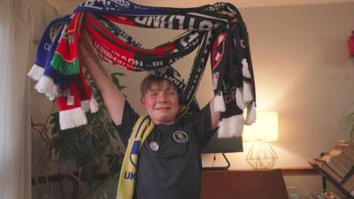 Child wearing Scotland football top and holding football scarves