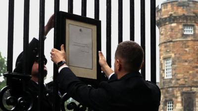 Two people place a notice on a gate