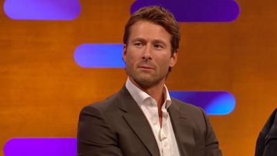 Glen Powell on the Graham Norton show wearing a brown suit and a white shirt