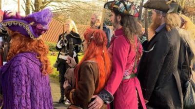 A number of pirates in colourful costumes stand outside a church.