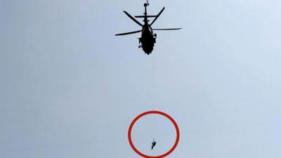 Helicopter flying with soldier hanging from rope attached to it