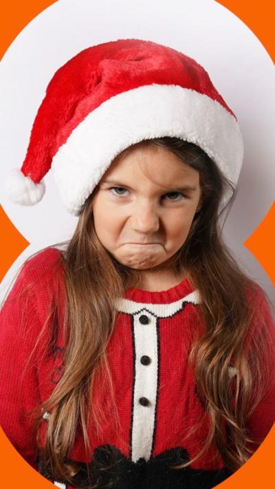A young girl dressed in a Santa's outfit looking very cross