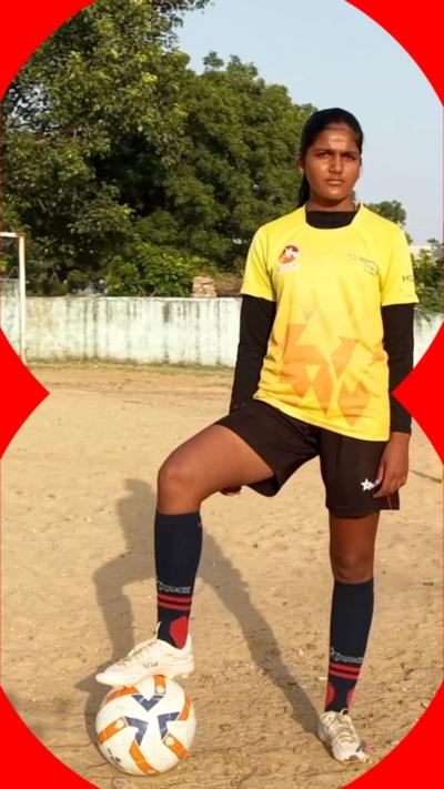 A girl wearing a yellow and black football kit stands with one foot on a football