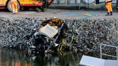 A badly damaged car is towed up from the canal under the E4 highway bridge in Sodertalje, Sweden