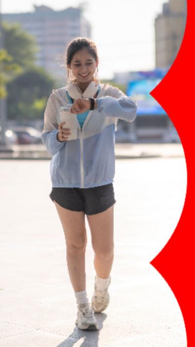 Woman wearing a rain coat and gym shorts walking whilst checking the time on her watch.