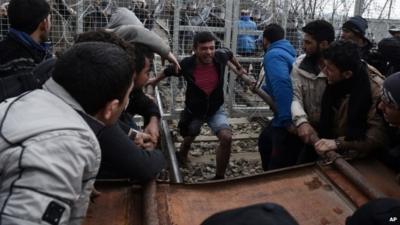 Refugees and migrants try to break an iron fence from the Greek side of the border as Macedonian police stand guard,