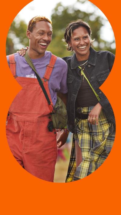 Two young people walking with their arms around each other and laughing, in colourful clothing