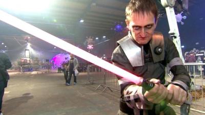 A man wearing a Star Wars outfit wields a toy lightsabre