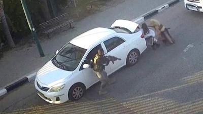 Two women take cover behind car as armed man stands next to car