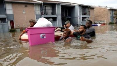 People move their belongings in a dinghy through a flooded street in Houston. The water is up to their chests.