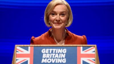 UK Prime Minister Liz Truss on stage in front of a lectern that says 'getting Britain moving'