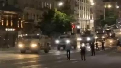 Train of armoured cars driving along a road in a built-up area of the city