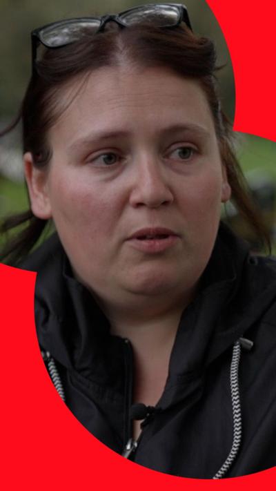 Women with dark hair wearing a black jacket interviewed at cemetery