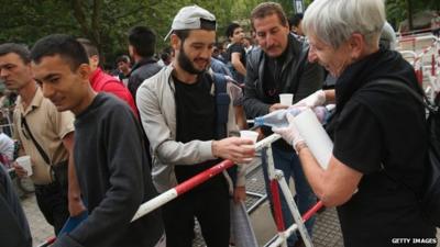 A volunteer distributes water to migrants seeking asylum in Germany and waiting to register at the Central Registration Office for Asylum Seekers