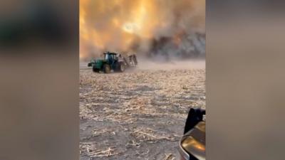 Tractor with wildfire burning behind it