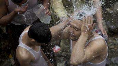 People cool themselves with a broken water pipeline in Islamabad, Pakistan as temperatures increased during Ramadan