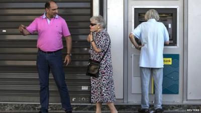 People stand next to an ATM outside a National Bank branch in Athens, Greece