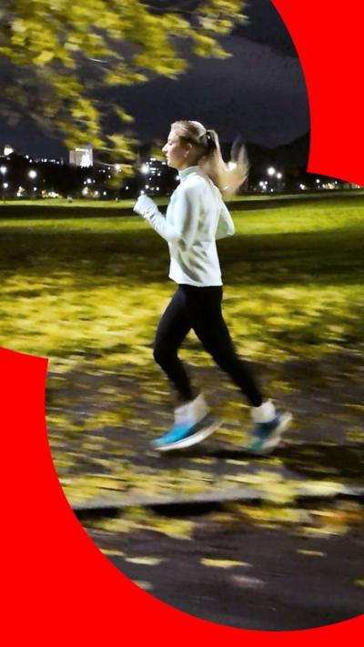 A woman with blonde hair and white top running in a park at night.
