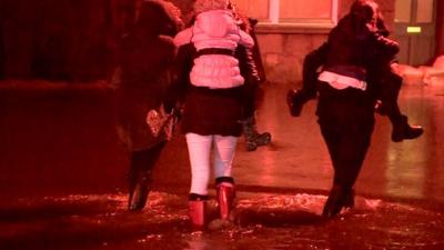 People carrying children in flooded street