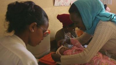 A baby being looked after by a mother and a healthcare worker