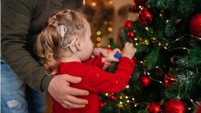 Girl with hearing aid decorating Christmas tree.