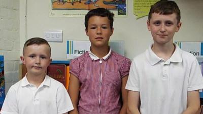 Three children stood in a row looking at the camera