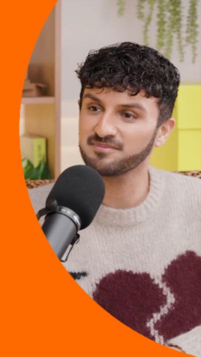 A man with short dark hair and a short dark beard speaks into a microphone while looking at someone off-camera