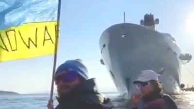 Protesters in a dinghy, waving a Ukrainian flag with the words "no war" written on it