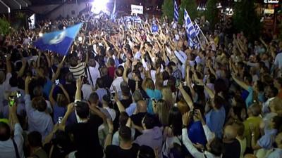 A crowd waves flags and phones in the air