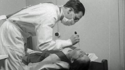 Doctor holding a pipette leans over patient lying back on a bed