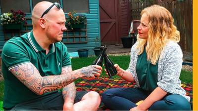 A man and woman toast with beer in a garden.