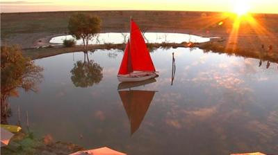 Wide shot of a small yacht in a very small lake with the horizon and sunset in the distance