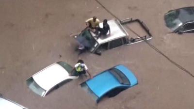 People sitting on the roofs of a cars in flood waters