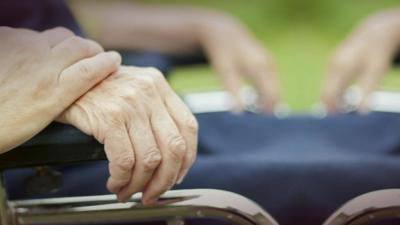Close up of of a younger hand holding an the hand of an older wheelchair user