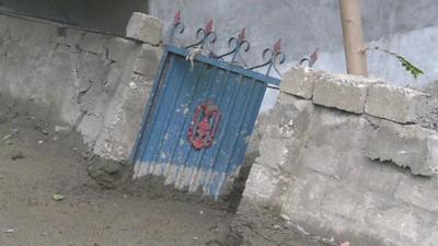 Mud from a flash flood piles up against a wall and gate to a compound