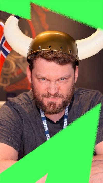 Bard Aune, BBC journalist, sat in a bar surrounded by viking paraphernalia, is pulling an angry face with viking horns on his head.