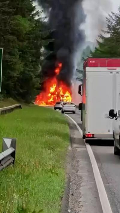 Lorry on fire on busy road beside a forest