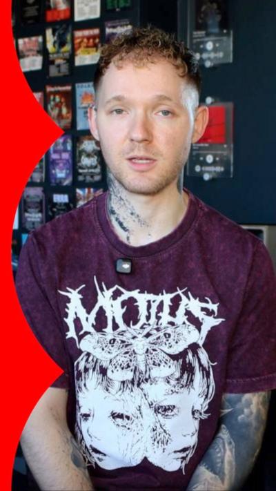 A man with a purple t-shirt and metal-style logo on the front. 