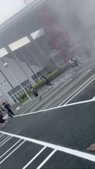 People flee from a building with smoke rising in the background