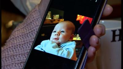 Pam Tooky holding a phone showing a picture of her grandson