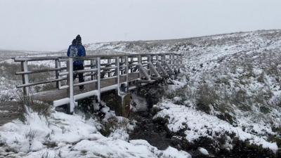 A man walks across a bridge in a snowy landscape