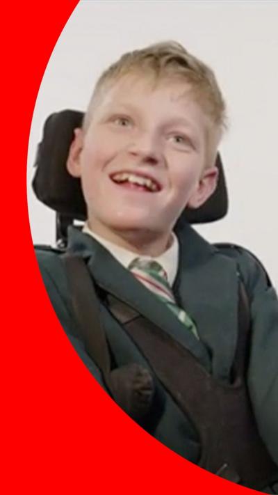 A boy wearing green school uniform smiling on an adapted wheelchair