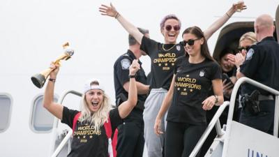 US Women's team exit the plane with their trophy