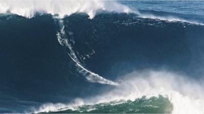 Surfer rides as big wave looms overhead