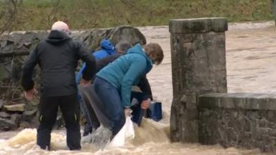 People attempting to block a gap in the wall to prevent floodwaters getting in