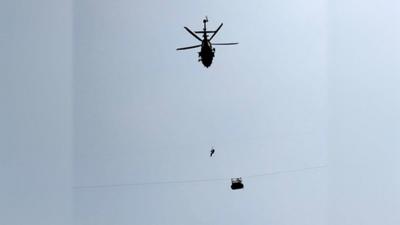 Army soldier slings down from a helicopter towards the cable