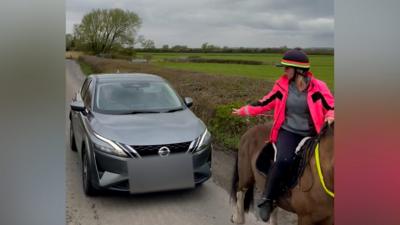 A video of a car driving close to a horse rider