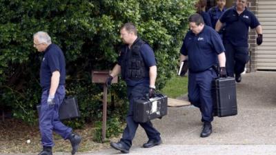 Officers carry equipment as they exit a house in Sydney